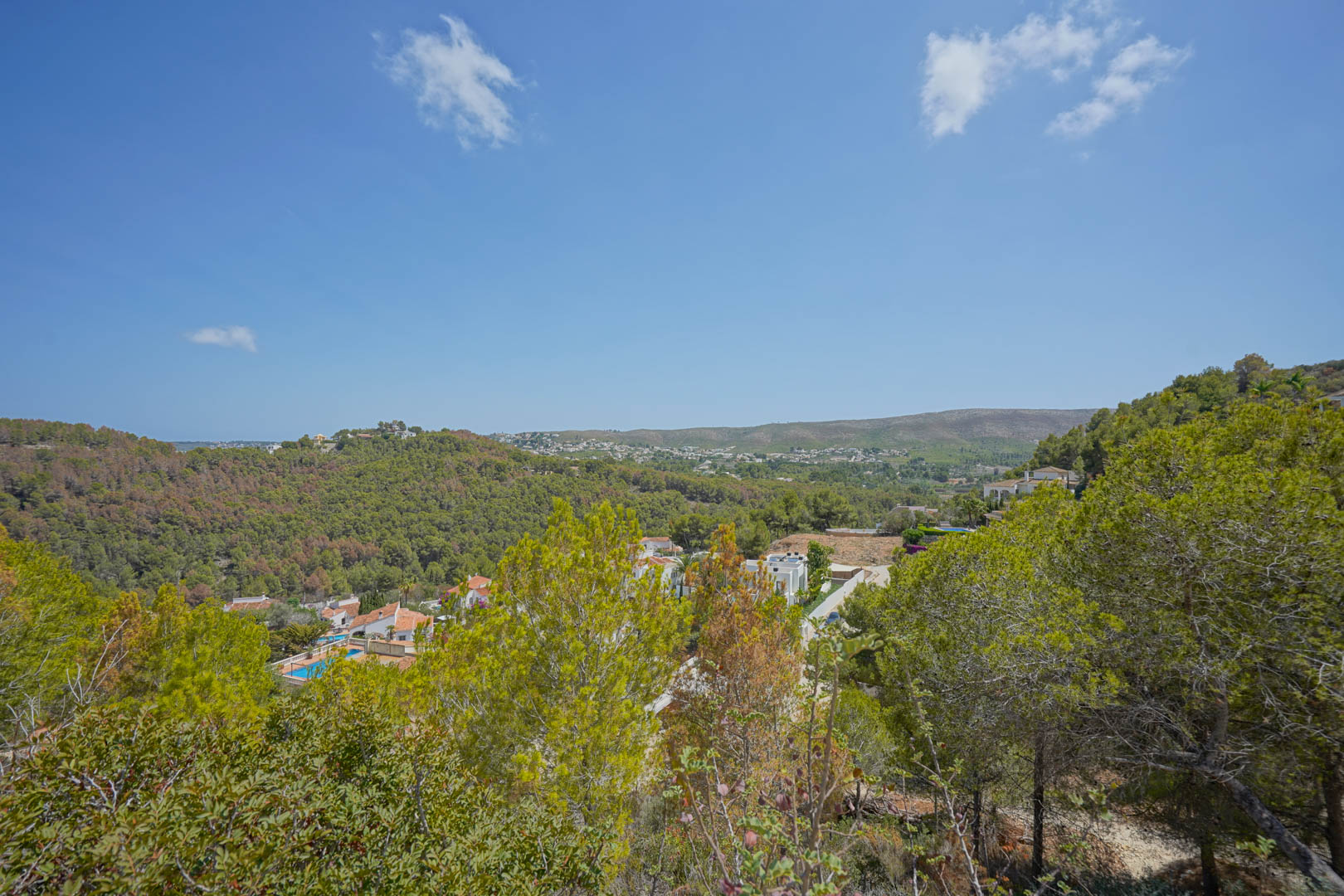 Panoramic view from the elevated plot overlooking the forested valley, residential villas, and the Mediterranean Sea horizon.