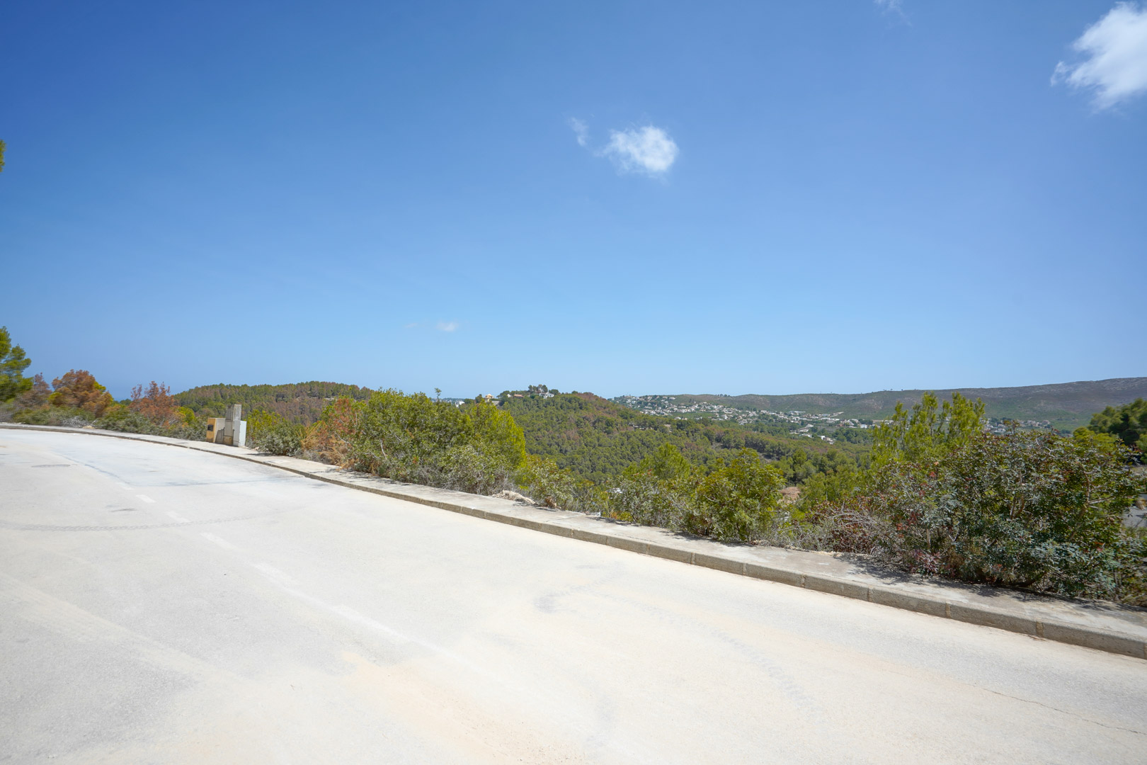 Panoramic view from the paved access road, featuring utility connections and unobstructed views of the surrounding green hills and Mediterranean landscape.