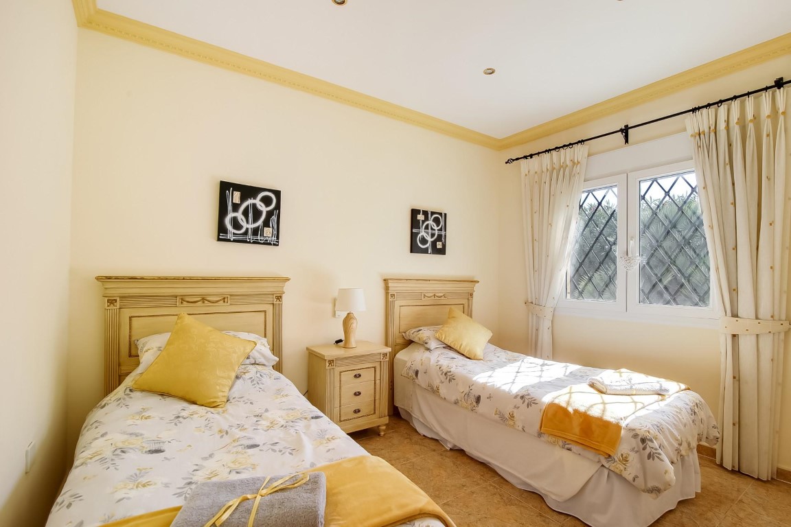 Bedroom featuring twin beds with classic wooden headboards, decorative crown molding, and a window with traditional diamond-patterned security bars.