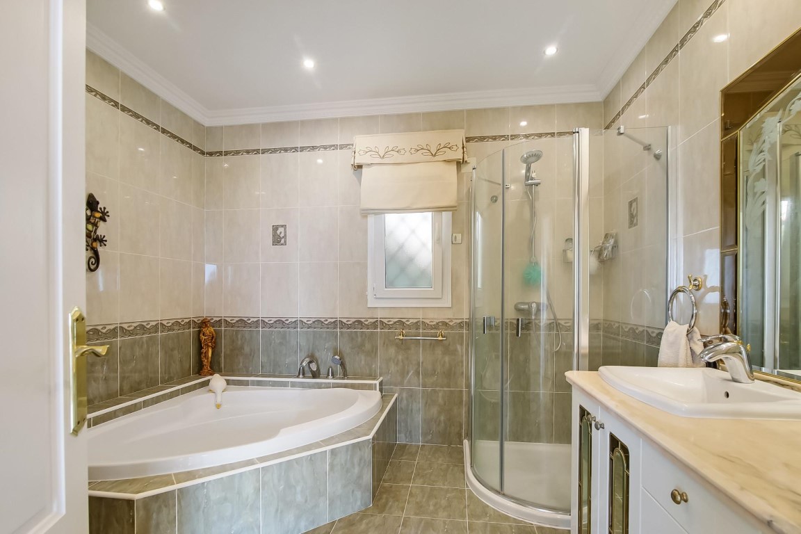 Full bathroom featuring a corner bathtub, curved glass shower enclosure, and marble-top vanity. Tiled walls with decorative borders and recessed ceiling spotlights.