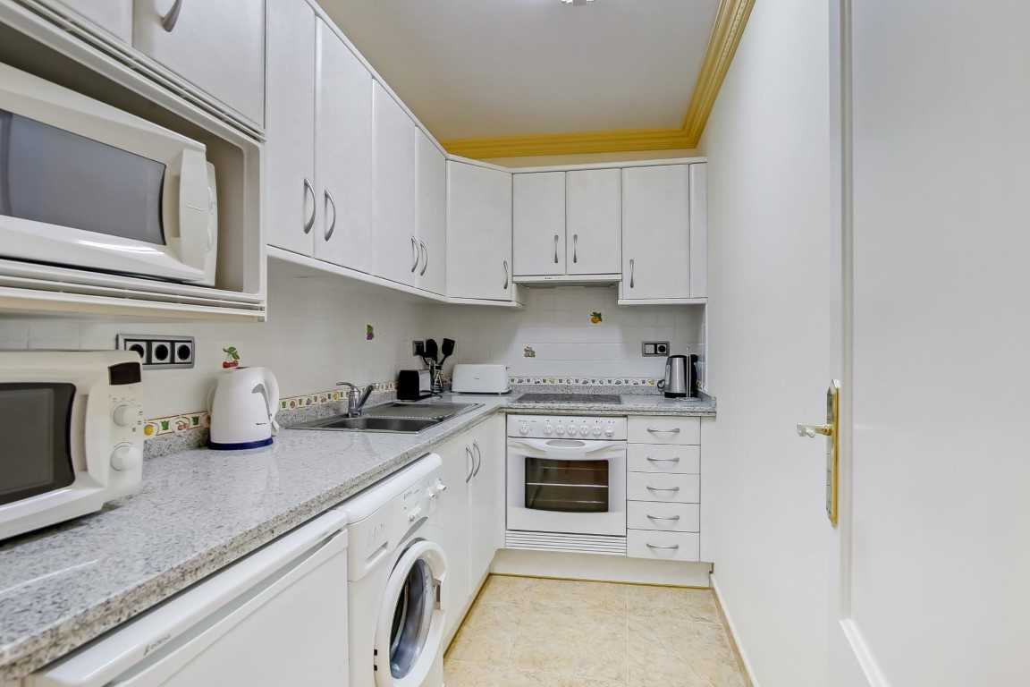 Functional kitchen featuring white cabinetry, grey granite countertops, and integrated appliances. It includes a built-in washing machine and decorative yellow ceiling molding.