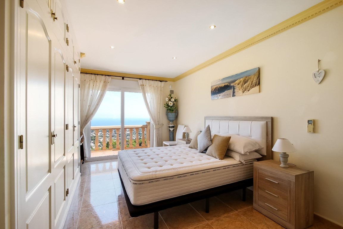 Master bedroom featuring floor-to-ceiling built-in wardrobes and sliding glass doors opening to a terrace with Mediterranean views.