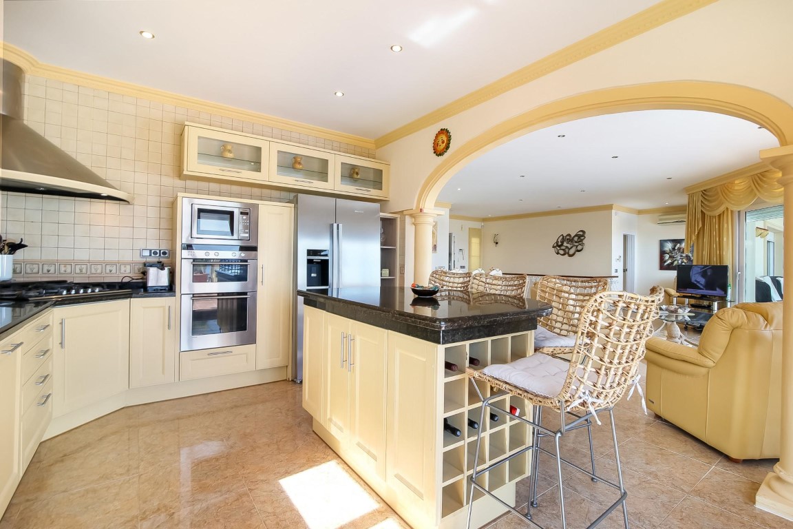 Open-concept kitchen featuring a dark granite island with wine storage, stainless steel appliances, and a classic archway leading to the living area.