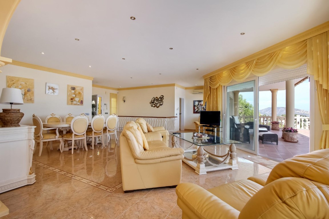 Open-plan living and dining area featuring polished tile floors, classic cream furniture, and large sliding doors opening onto a scenic terrace.