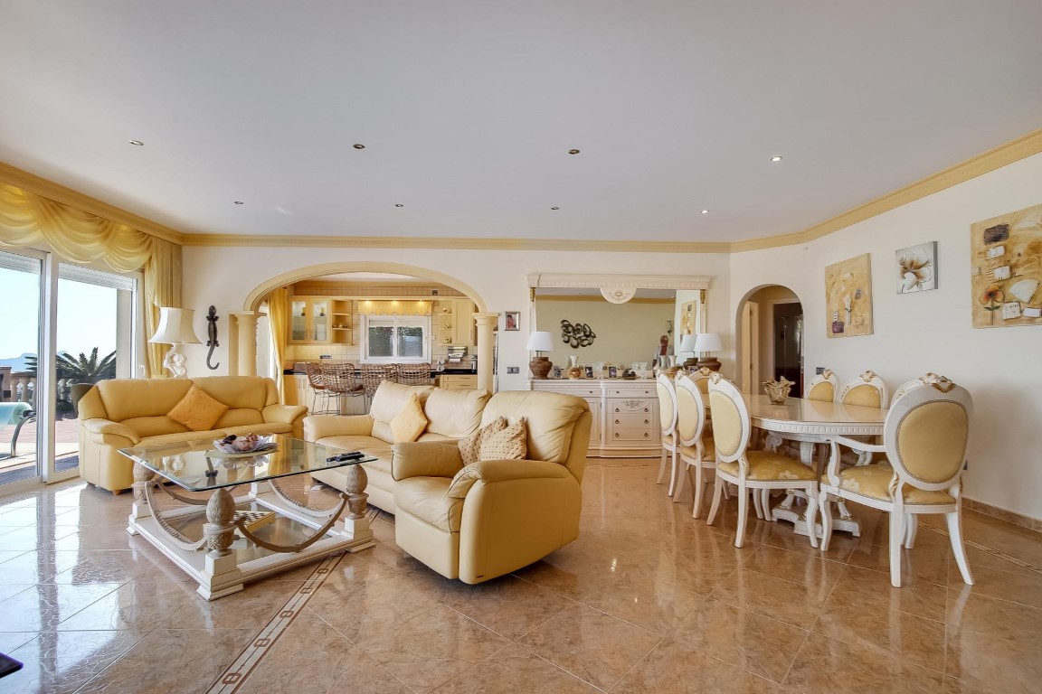 Open-plan living and dining area featuring polished tile floors with decorative borders, classic cream furniture, and an elegant archway leading to the kitchen.
