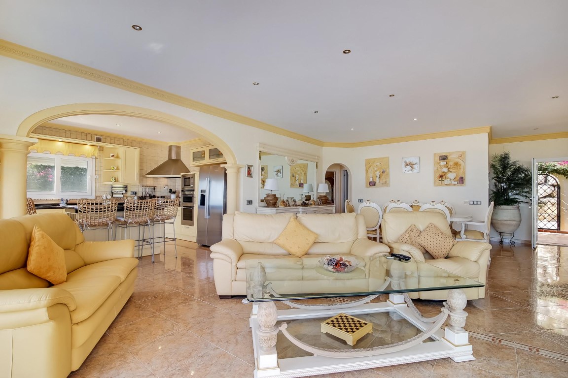 Open-plan living area featuring leather seating, polished stone floors, and a wide archway leading to a fully equipped kitchen with a breakfast bar.