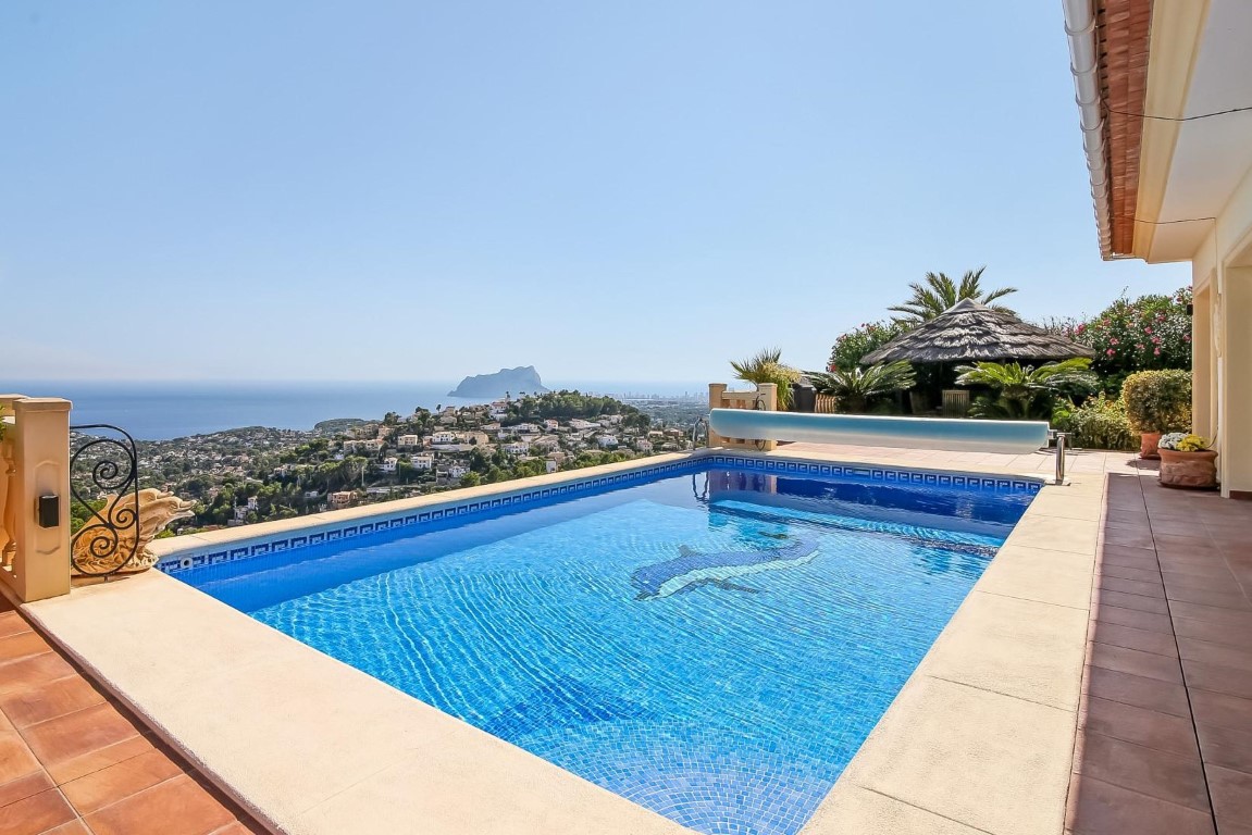 Outdoor swimming pool featuring a dolphin mosaic and panoramic views of the Mediterranean Sea and Peñón de Ifach, set on a terracotta terrace.
