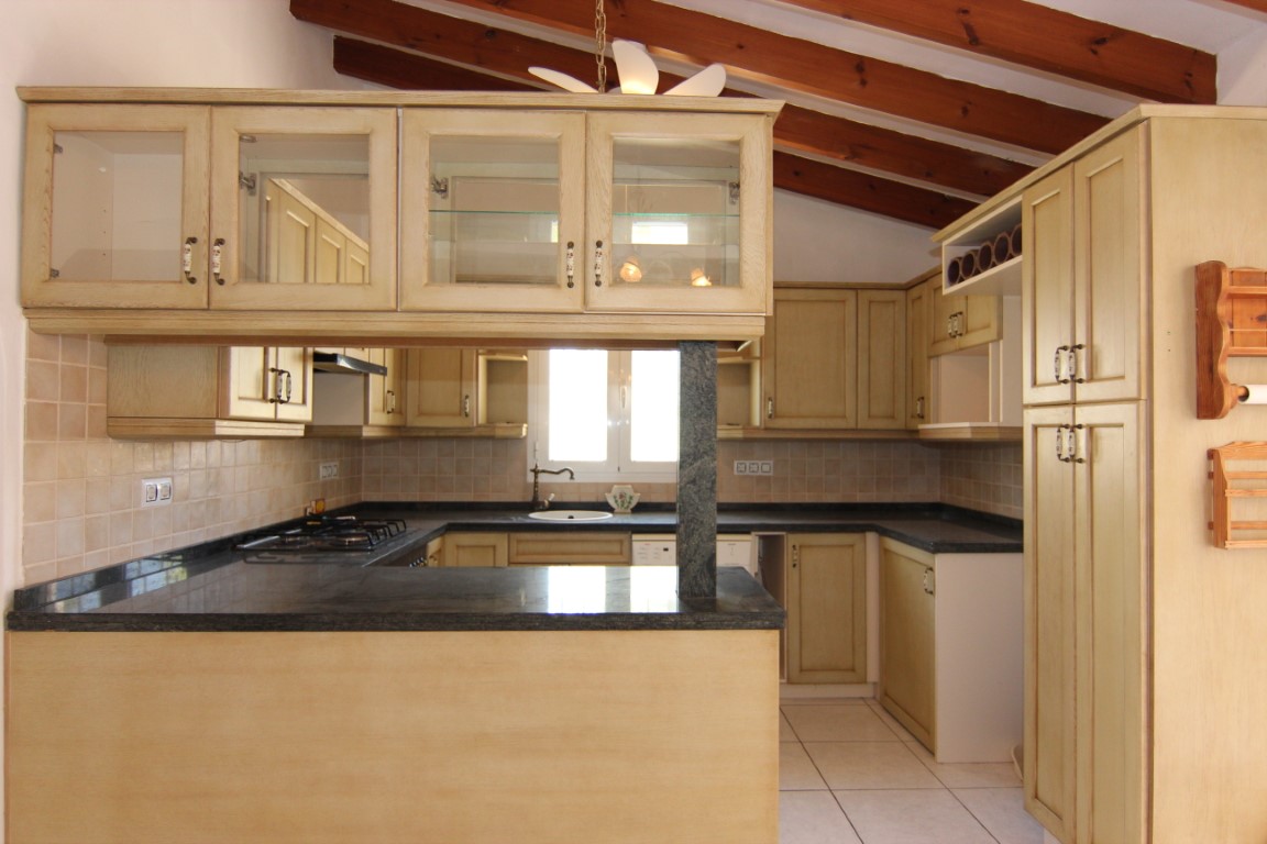 Rustic-style kitchen featuring exposed wooden ceiling beams, dark granite countertops, and cream cabinetry with glass displays and a functional breakfast bar.