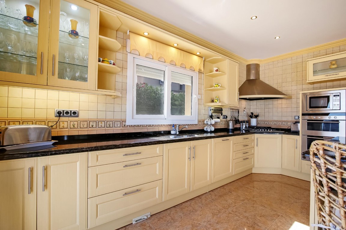 Traditional kitchen featuring cream cabinetry, dark granite countertops, and integrated stainless steel appliances with recessed spotlighting and tiled backsplash.