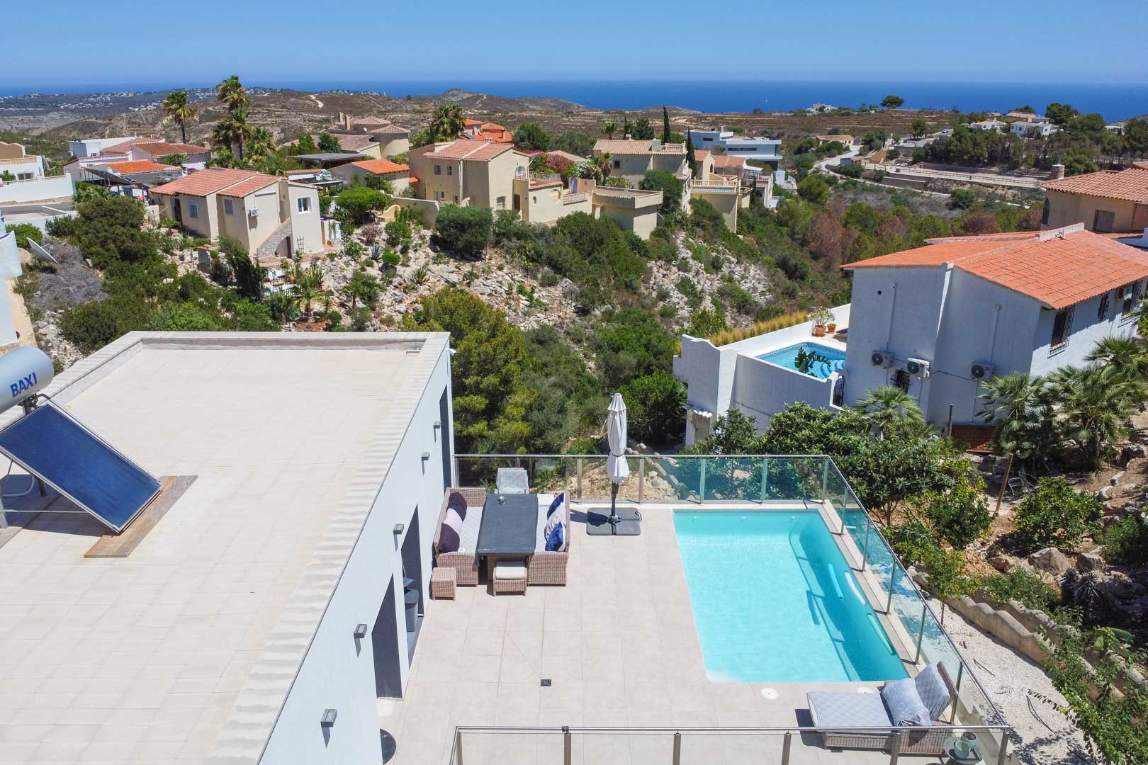 Aerial view of the terrace featuring a rectangular pool, glass balustrades, and outdoor dining. The flat roof shows the solar heater overlooking the Mediterranean Sea.