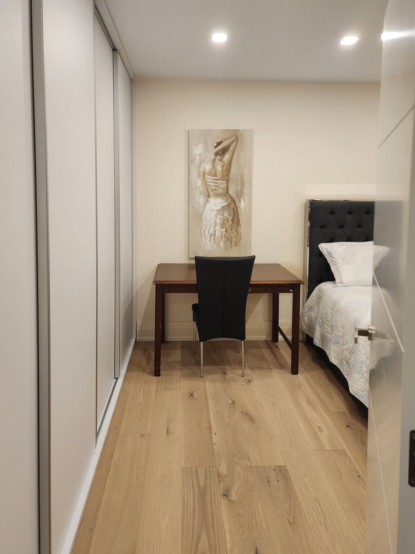 Bedroom featuring floor-to-ceiling built-in wardrobes, a wooden desk workspace, and oak flooring illuminated by recessed ceiling spotlights.