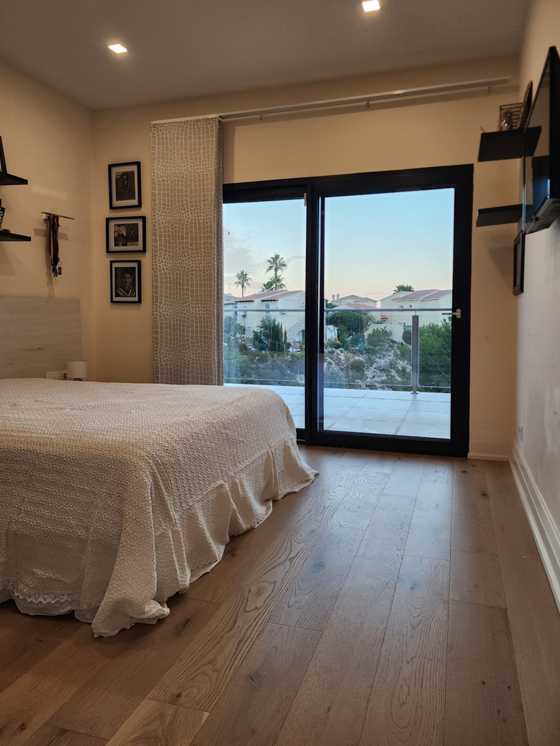 Bedroom featuring natural wood flooring, recessed ceiling lighting, and large sliding glass doors opening onto a terrace with views of the surrounding landscape.