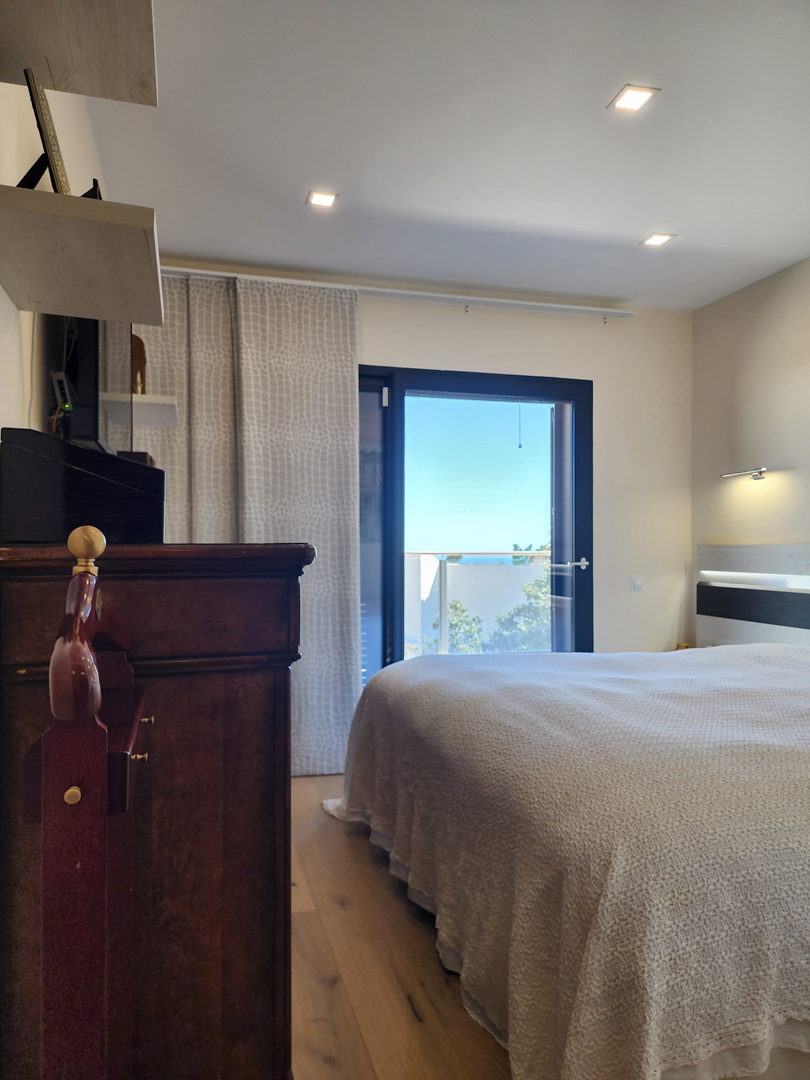Bedroom featuring wooden flooring, recessed ceiling lights, and direct access to a terrace with sea views through a dark-framed glass door.