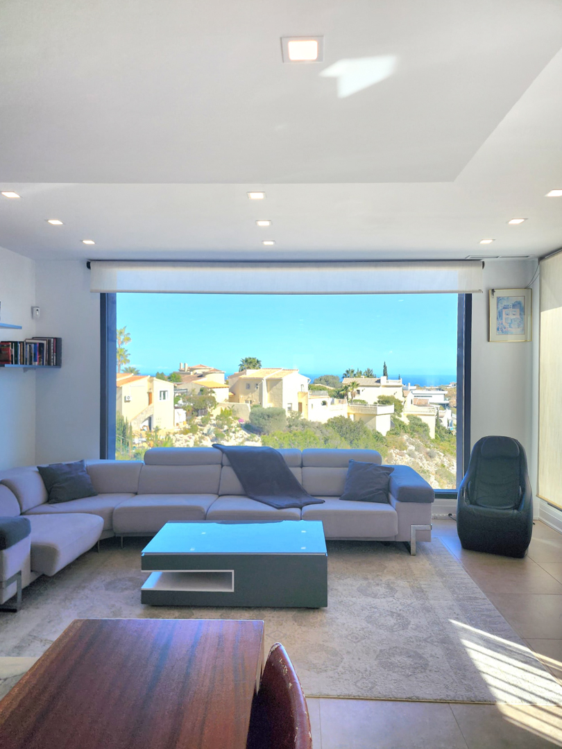 Bright living area featuring a large picture window with coastal views, a grey sectional sofa, and integrated ceiling spotlights for a modern aesthetic.