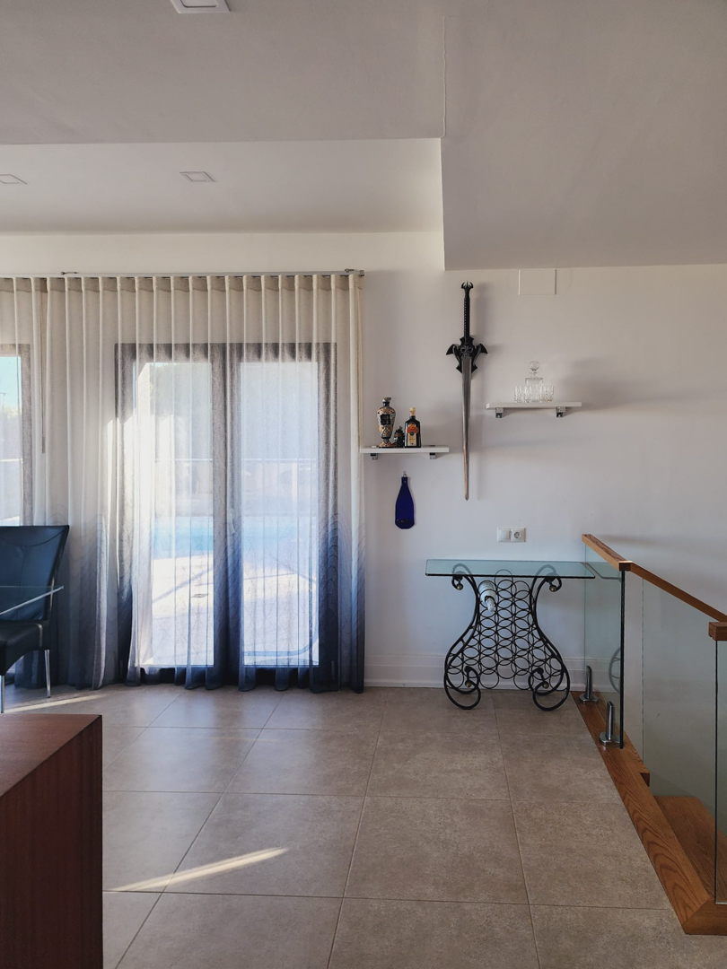 Bright living area featuring porcelain tile flooring, a decorative glass console table, and a modern staircase with a glass balustrade and wooden accents.