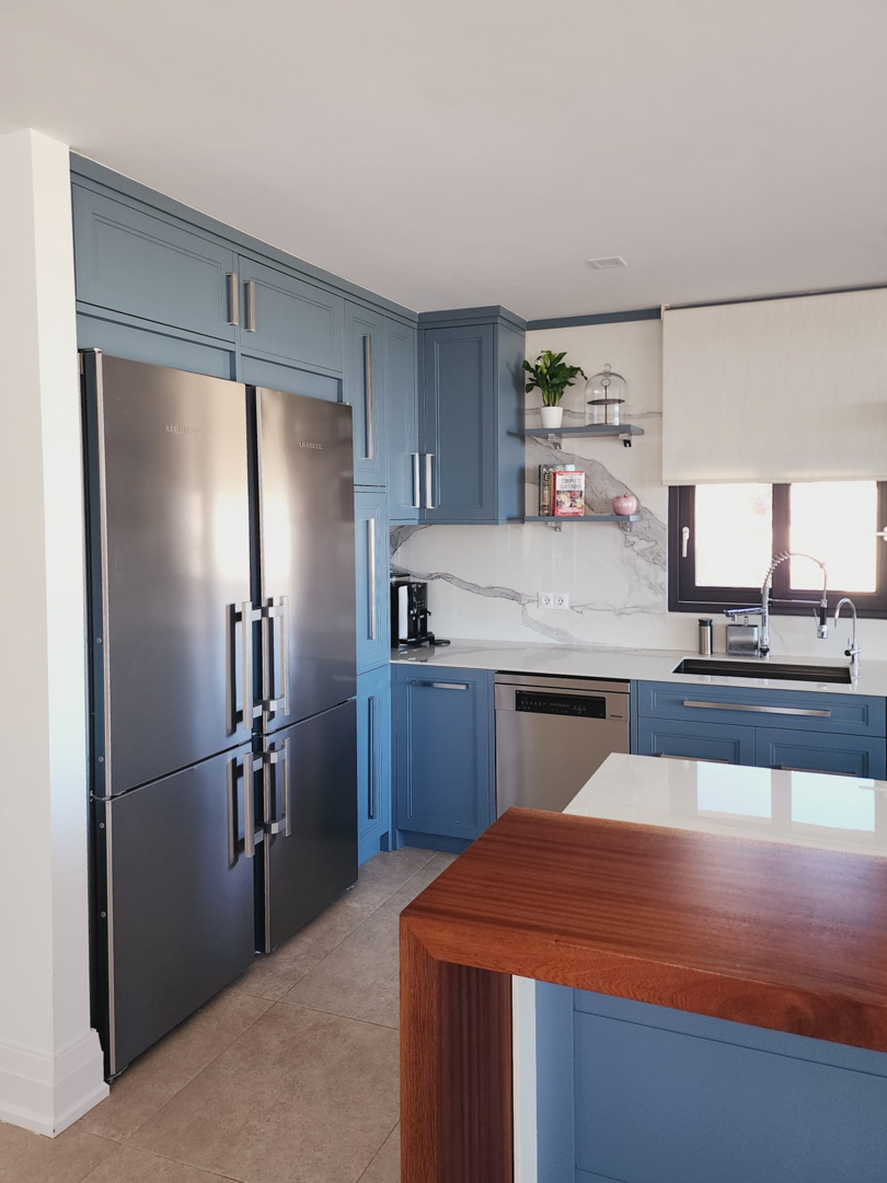 Designer kitchen featuring blue cabinetry, marble-effect backsplash, and high-end stainless steel appliances. A solid wood breakfast bar complements the white countertops.