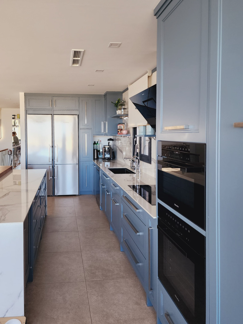 Designer kitchen featuring blue-grey cabinetry, marble-effect countertops, and integrated Miele appliances, including double ovens and a large stainless steel refrigerator.