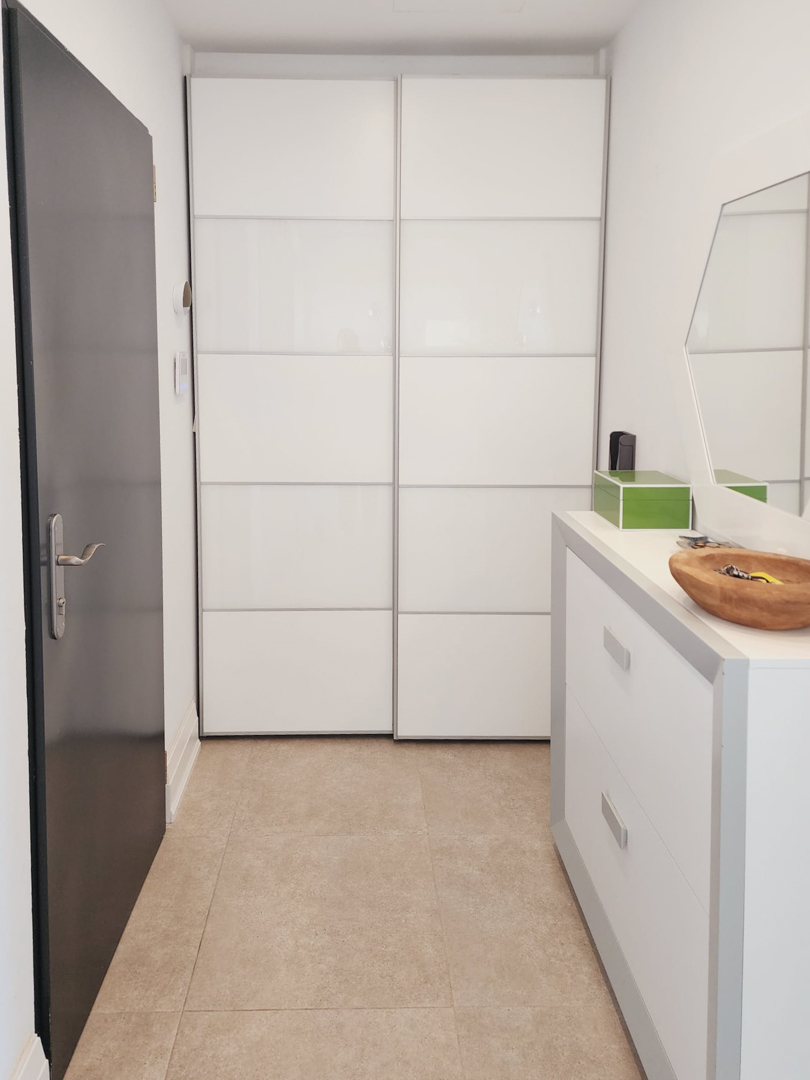 Entrance hall featuring a modern built-in wardrobe with white sliding panels, a sleek chest of drawers, and neutral tiled flooring.