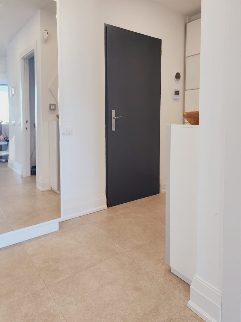 Entrance hallway featuring large format floor tiles, a floor-to-ceiling mirror, and a minimalist dark door contrasting with crisp white walls.