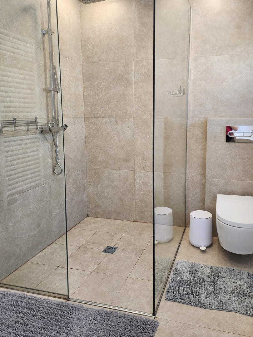 Modern bathroom featuring a walk-in shower with a glass screen, sand-toned porcelain tiling, and a wall-hung toilet with sleek chrome fixtures.
