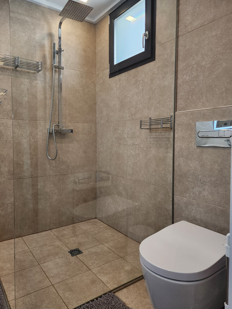Modern bathroom featuring a walk-in shower with glass partition, chrome rain shower head, and neutral sand-toned ceramic tiling throughout.