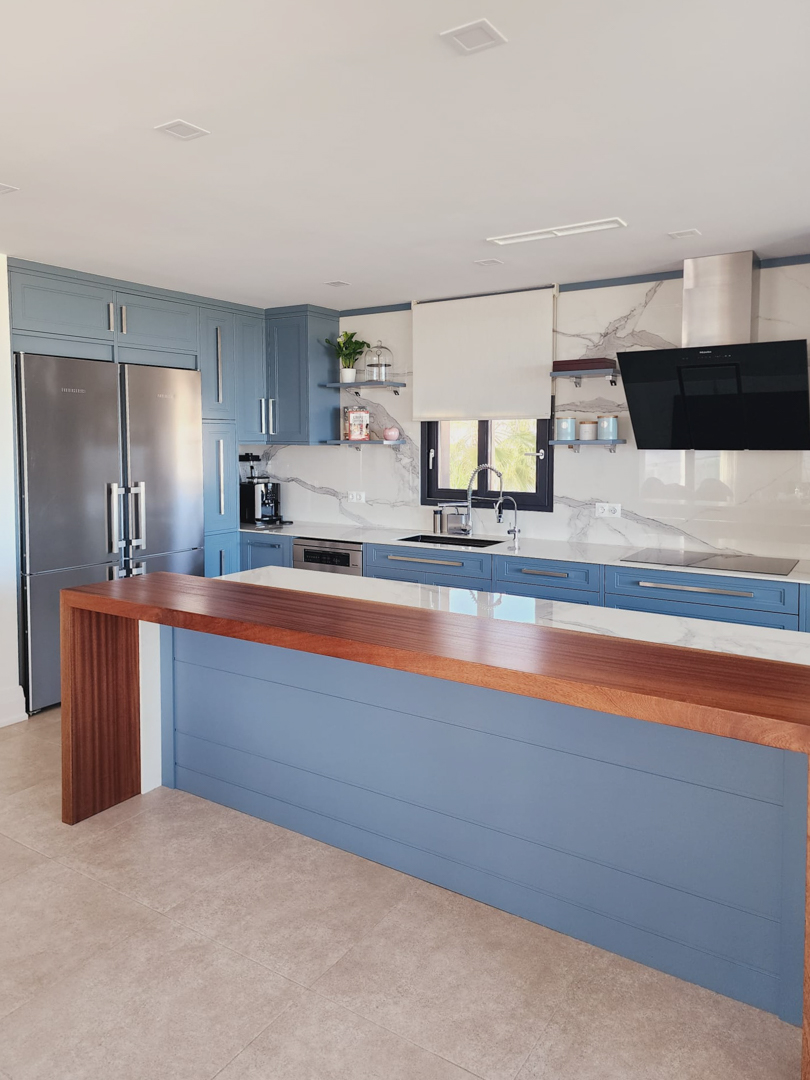 Modern kitchen featuring blue cabinetry, marble-effect surfaces, and a solid wood breakfast bar. It includes integrated appliances and a spacious, bright workspace.