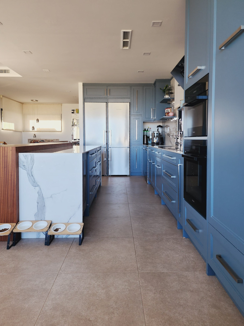 Modern kitchen with pastel blue cabinetry, a marble-veined central island, and integrated Miele appliances. Features porcelain tile flooring and recessed lighting.