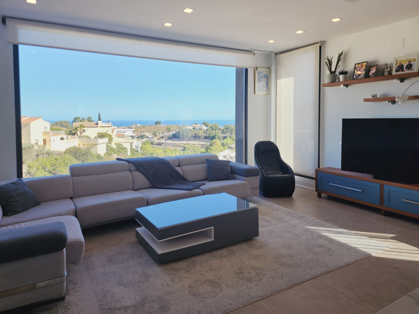 Modern living room featuring a large panoramic window with sea views, an L-shaped sofa, designer coffee table, and recessed ceiling lighting.