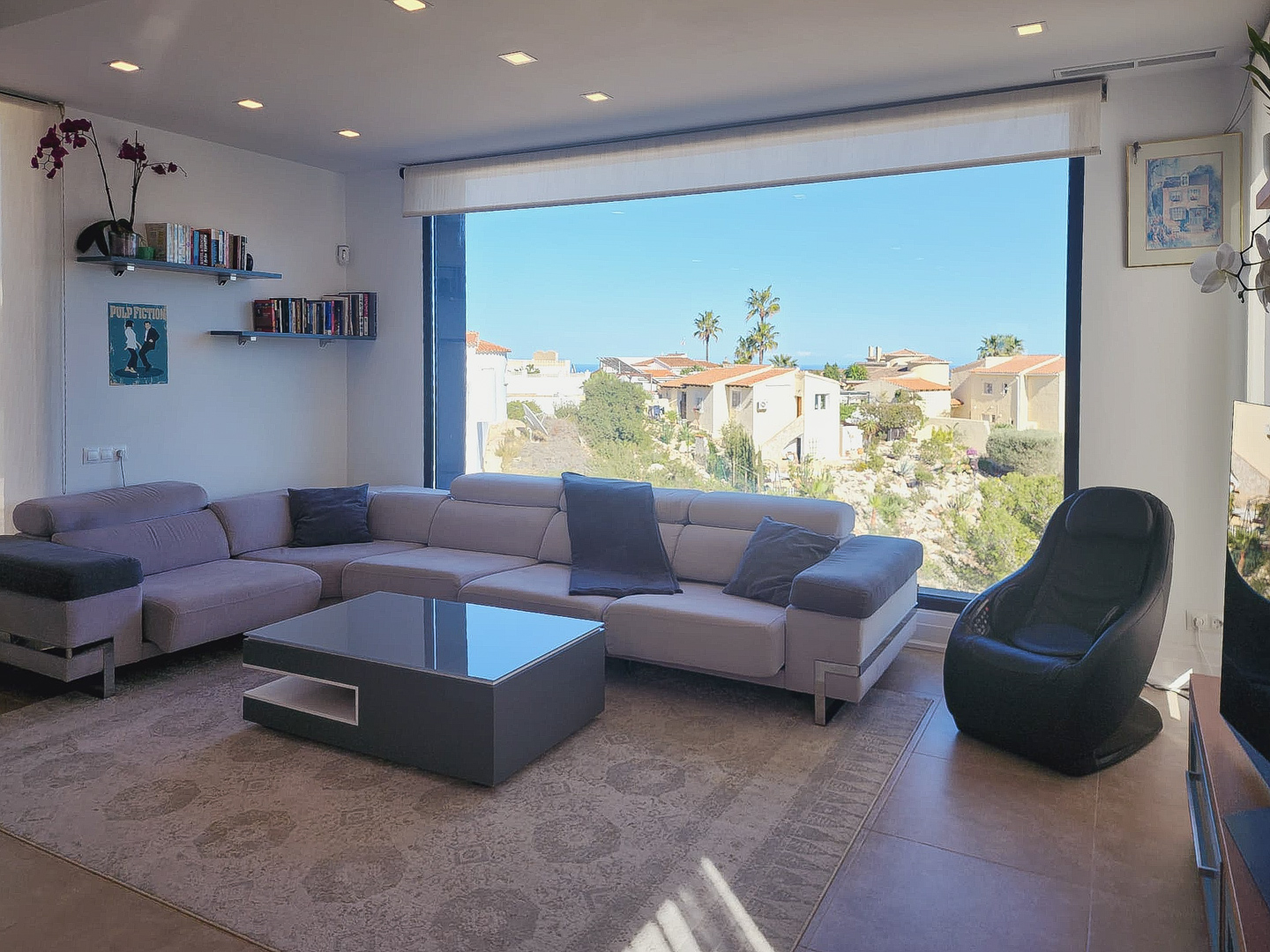 Modern living room featuring an L-shaped sofa, minimalist coffee table, and a large picture window. Includes recessed ceiling lights and views of the surrounding landscape.