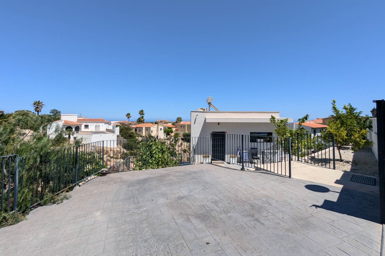 Outdoor parking area featuring grey stamped concrete flooring and black metal railings, overlooking the surrounding Mediterranean residential landscape.