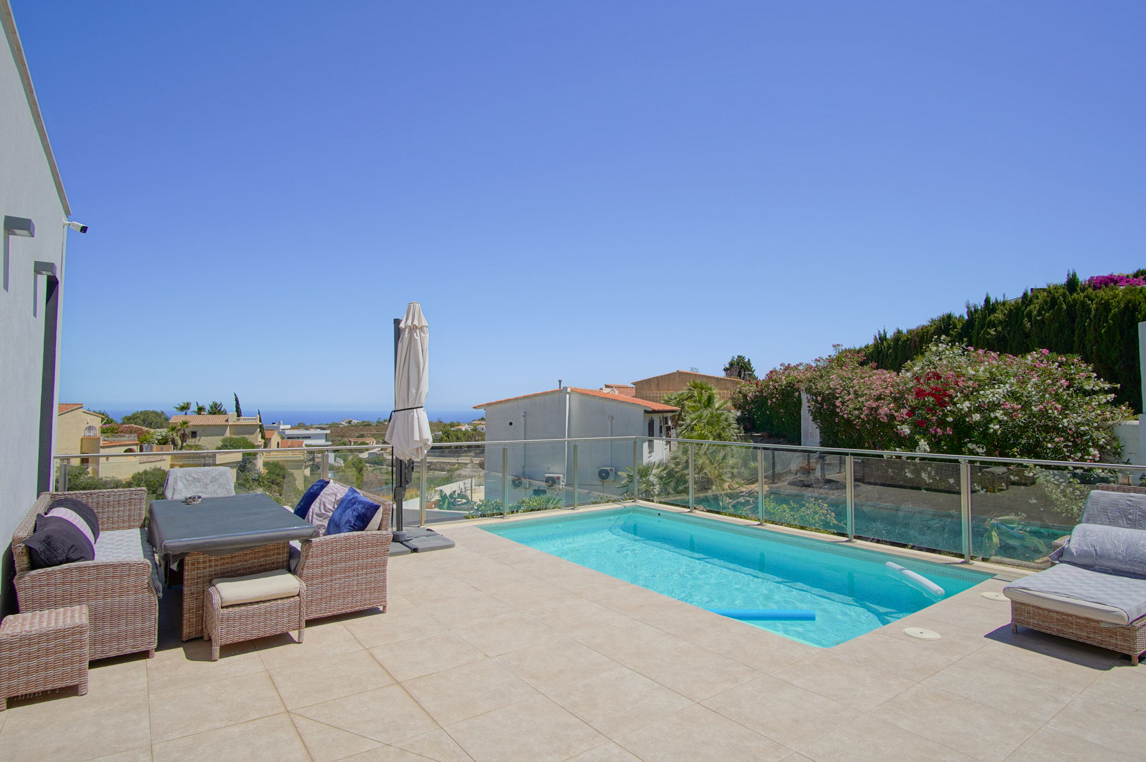 Outdoor terrace featuring a rectangular swimming pool, glass railings, and wicker lounge furniture. The south-facing area provides clear sea views and ample sun.