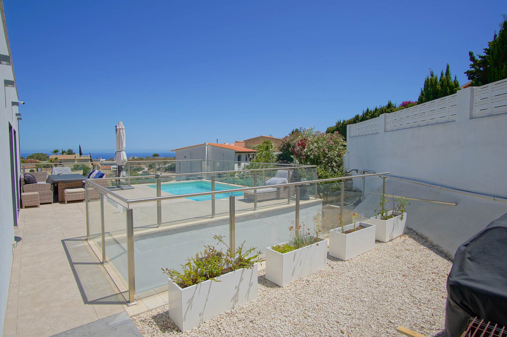 Outdoor terrace featuring glass and steel balustrades, a swimming pool with sun deck, and a gravel area with modern white planters.