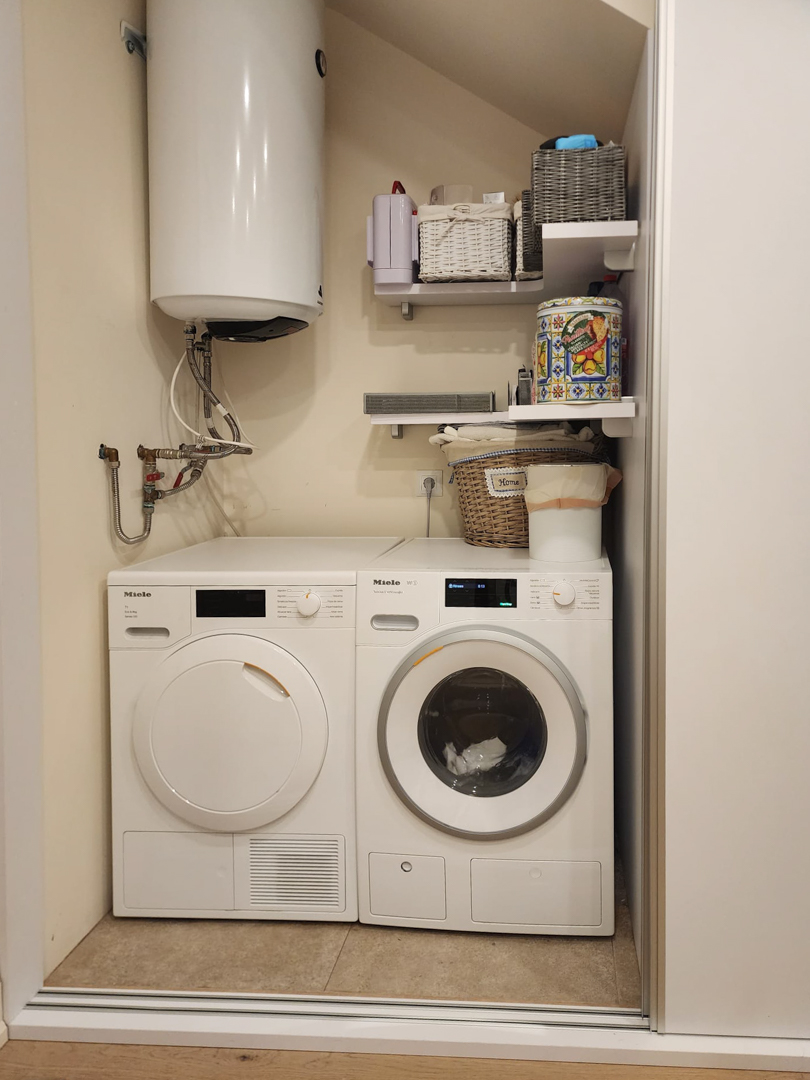 Utility area featuring Miele laundry appliances, a wall-mounted solar water heater, and integrated shelving for storage.
