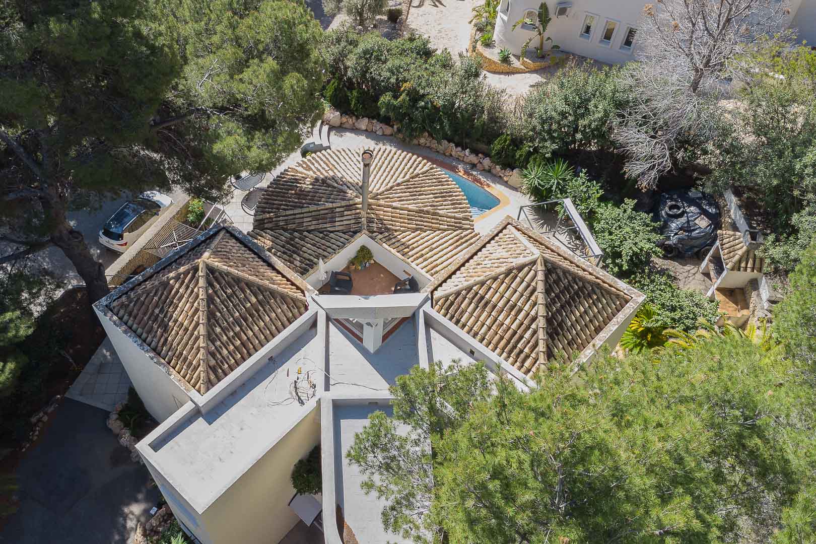 Aerial view showcasing the villa's unique architectural design with pyramidal tiled roofs, a central chimney, and an integrated upper terrace surrounded by lush greenery.