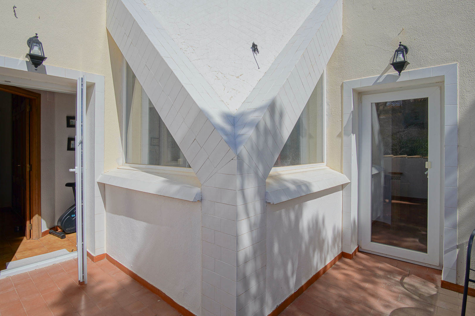 Architectural detail of the upper terrace featuring white-tiled pillars, terracotta flooring, and glass door access to the interior rooms and fitness area.