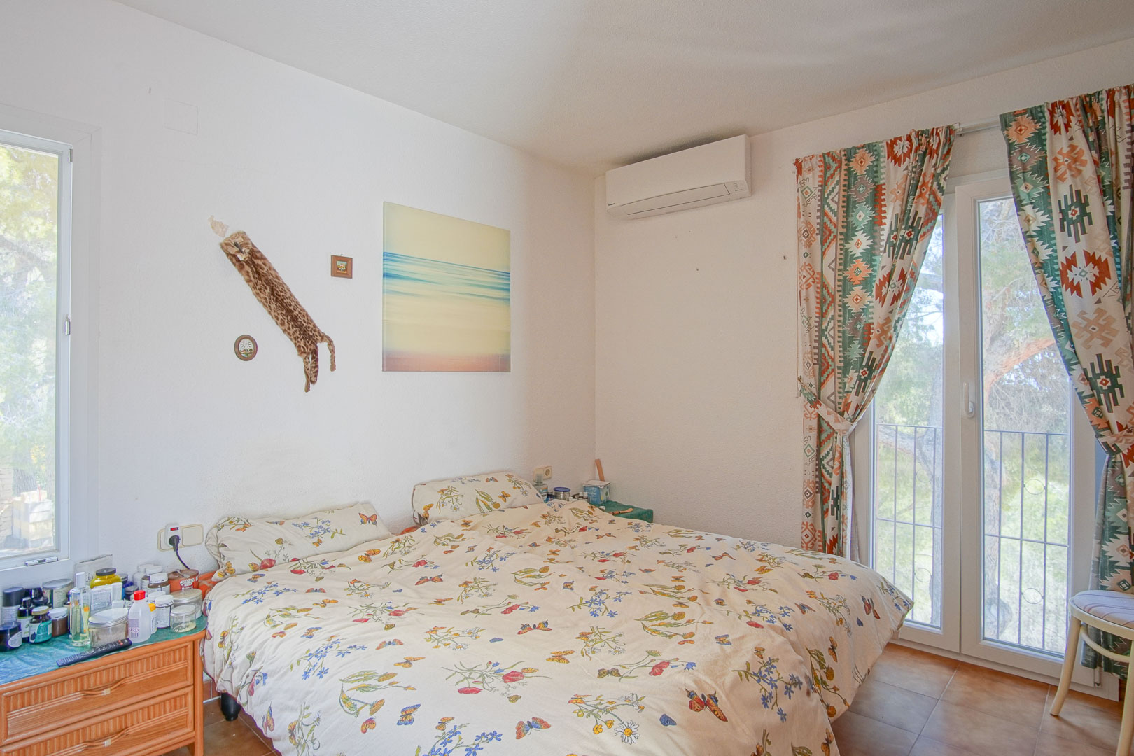 Bright bedroom featuring a split air conditioning unit, direct terrace access through glass doors, and rustic tile flooring.