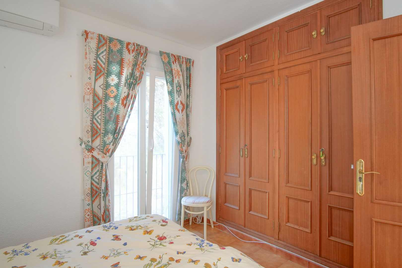 Bright bedroom featuring floor-to-ceiling wooden built-in wardrobes, split-system air conditioning, and a glass door providing natural light and outdoor access.