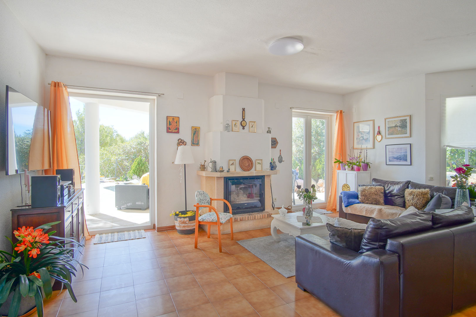 Bright living room featuring a central fireplace, terracotta tile flooring, and direct access to the outdoor porch through large glass doors.