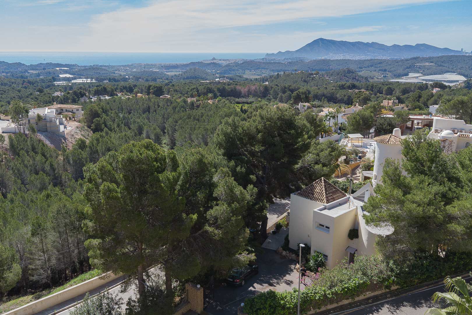 Elevated panoramic view showcasing the villa nestled among pine trees, offering clear vistas of the Mediterranean Sea and surrounding mountains.