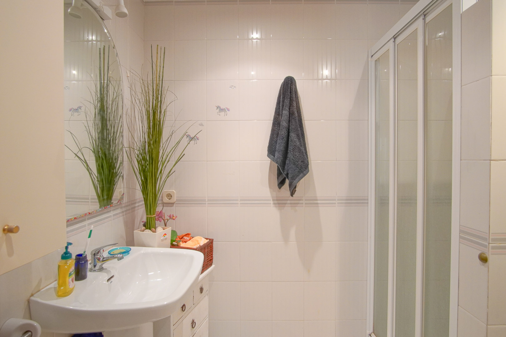 Functional bathroom featuring white tiled walls, a porcelain washbasin, an arched mirror, and a shower area with a white sliding door.