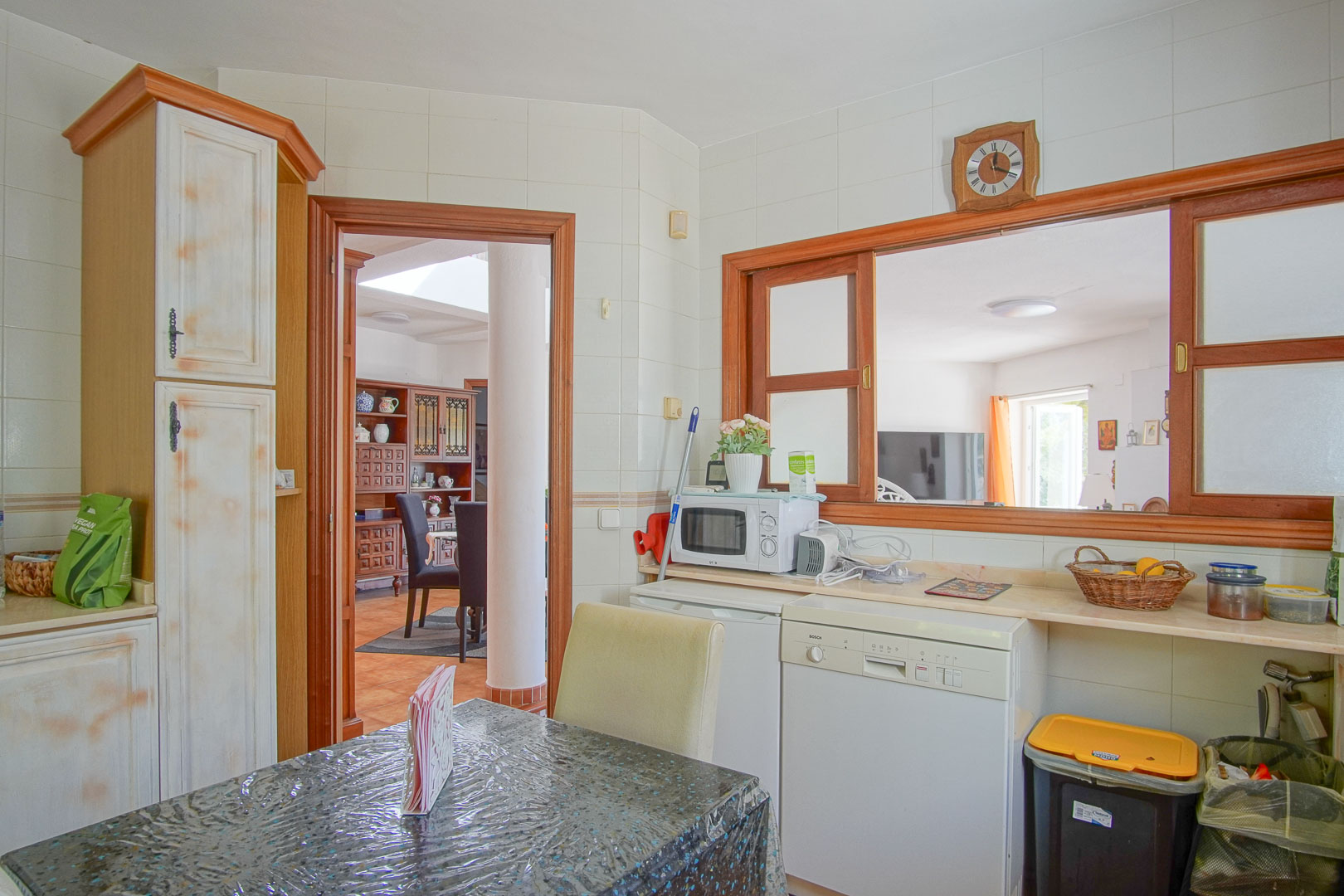 Independent kitchen featuring rustic cabinetry, a breakfast area, and a pass-through window to the dining room. Equipped with a dishwasher and light-toned countertops.