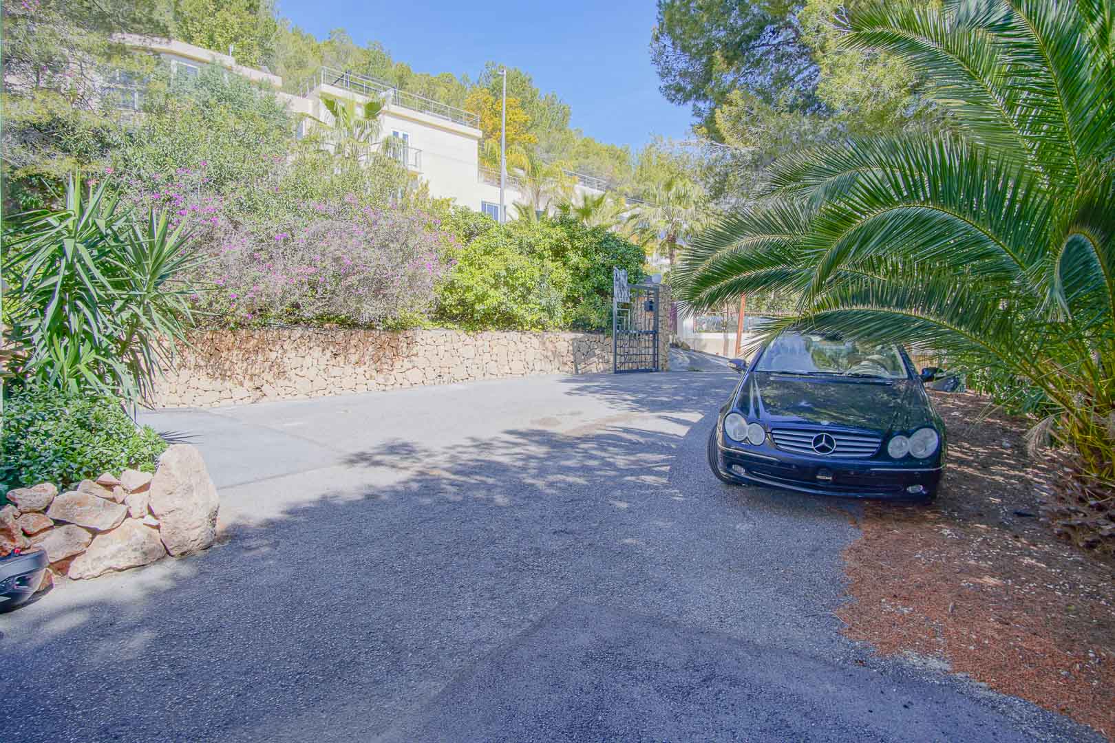 Spacious paved outdoor parking area bordered by natural stone walls and mature Mediterranean greenery, offering ample room for several vehicles.
