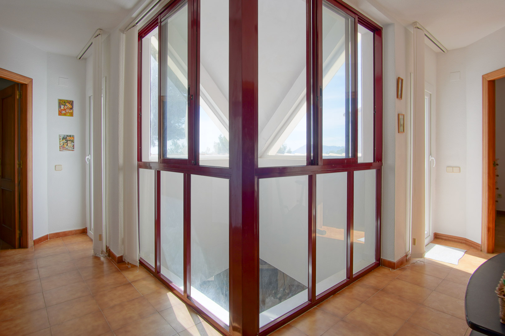 Upper floor landing featuring a distinctive corner glass enclosure with burgundy frames, terracotta tiling, and bright natural light throughout the hallway.