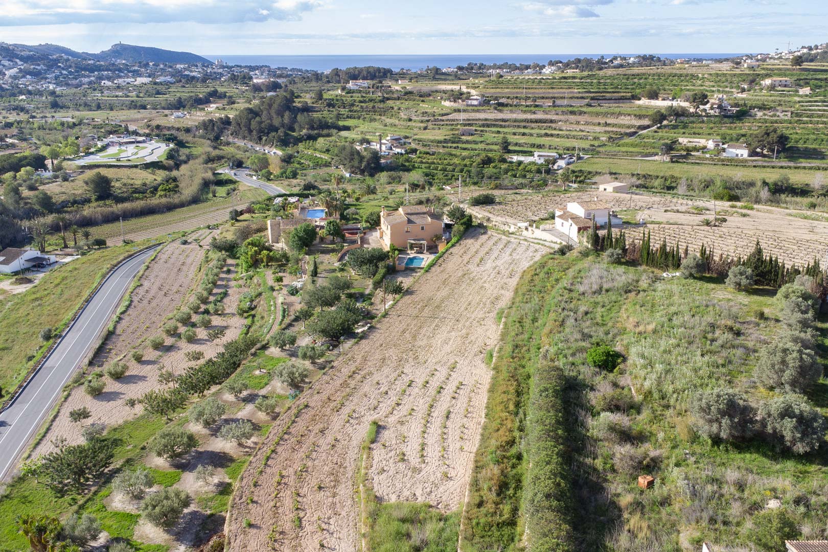 Aerial view of the expansive 10,920 m2 plot in Teulada-Moraira, featuring terraced agricultural land and panoramic views toward the Mediterranean coastline.