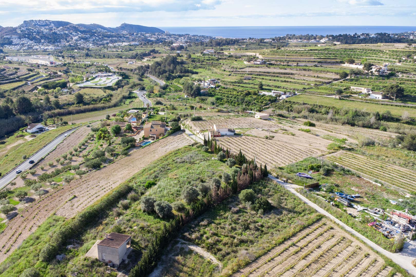 Aerial view of the expansive 10,920 m2 rustic plot in Teulada-Moraira, featuring terraced agricultural land and distant Mediterranean Sea views.