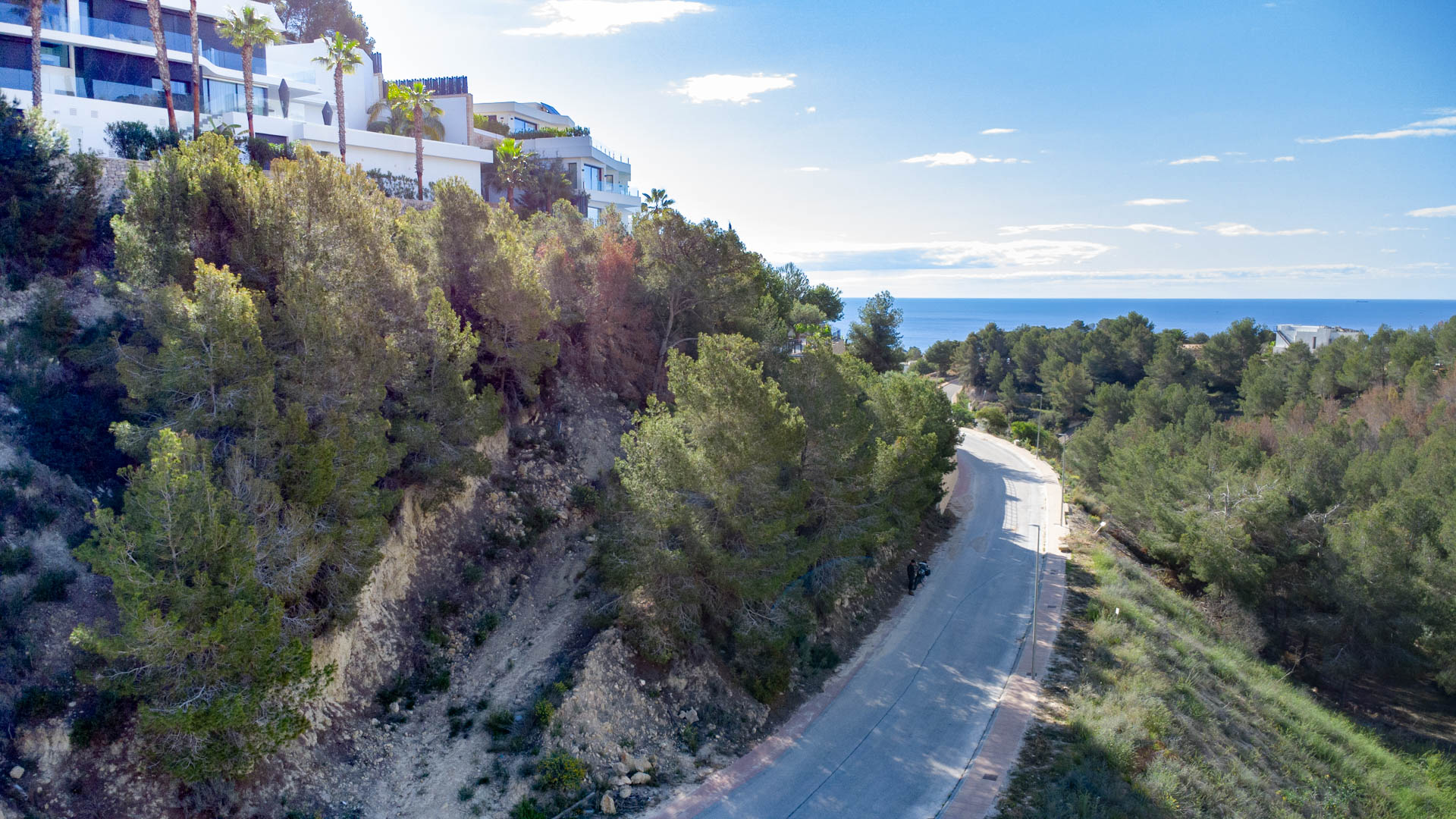 Elevated view of the access road in Racó de Galeno, showing the pine-covered hillside and modern villas overlooking the Mediterranean Sea.