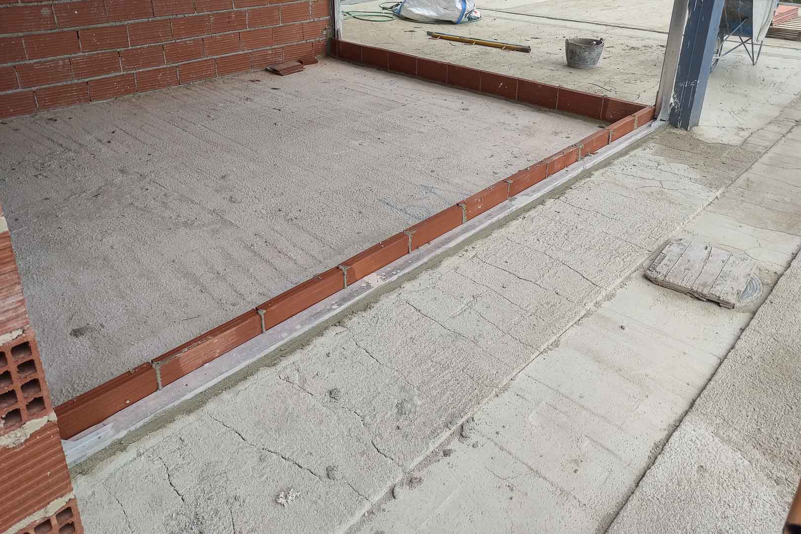 Construction phase: detail of the concrete subfloor leveling and pre-installation of metal tracks for the large sliding glass doors.