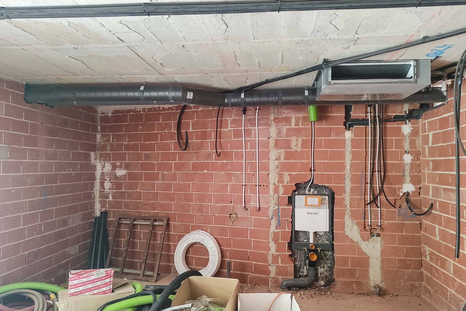 Construction phase detail showing the aerothermal HVAC ductwork installation and a wall-mounted toilet cistern frame integrated into the brickwork.