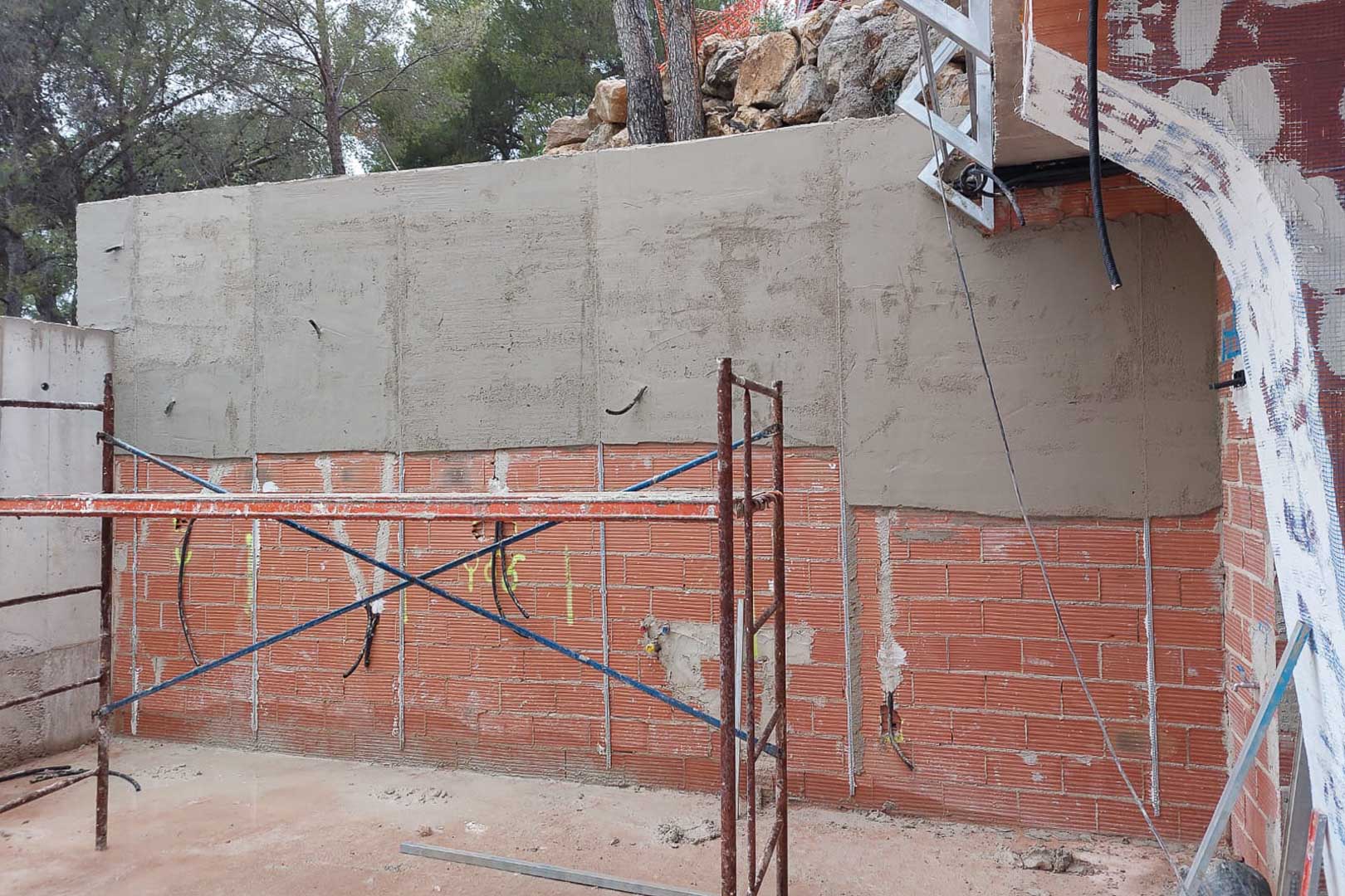 Construction phase showing brick wall rendering, electrical pre-installations, and technical scaffolding on the villa's exterior structure.
