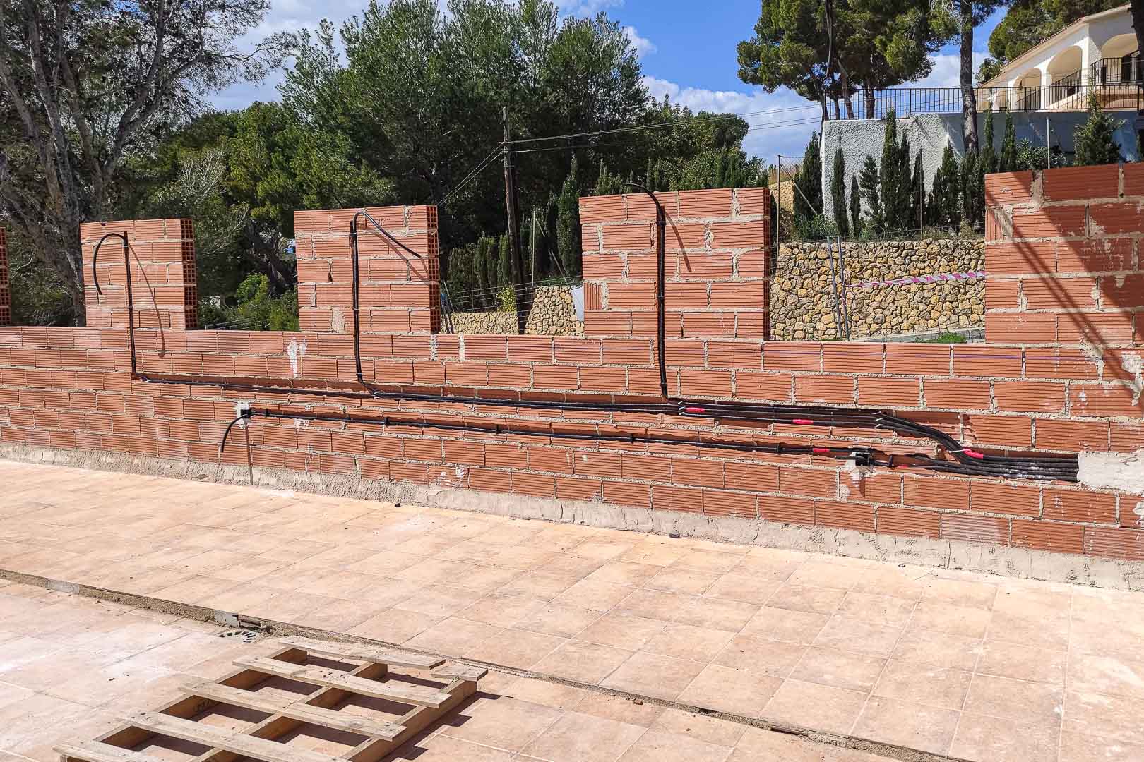 Construction phase showing electrical conduit installation on brick perimeter walls, preparing for integrated outdoor lighting and security systems.